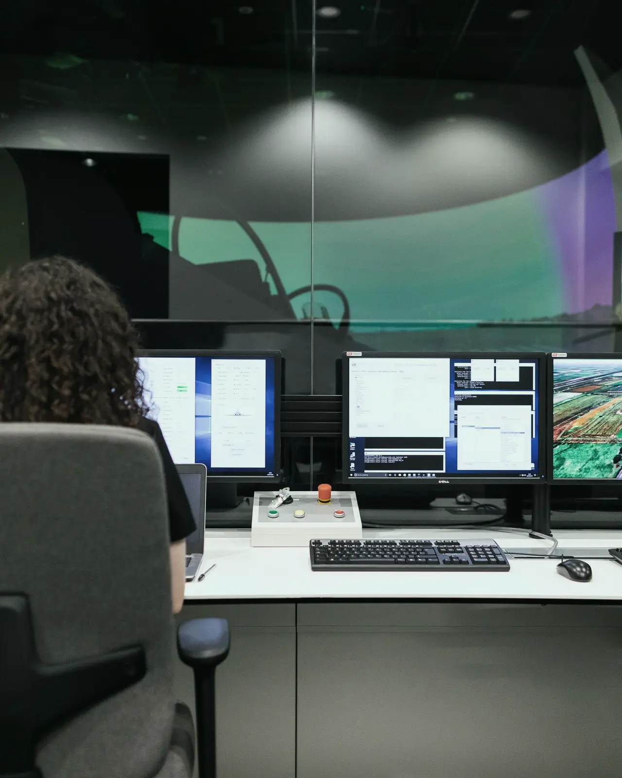 An analyst at her console in an operations center, monitors and a large wall display in front of her